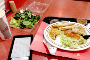 Taquitos, salad, coke and kindle on the table at burgurshop