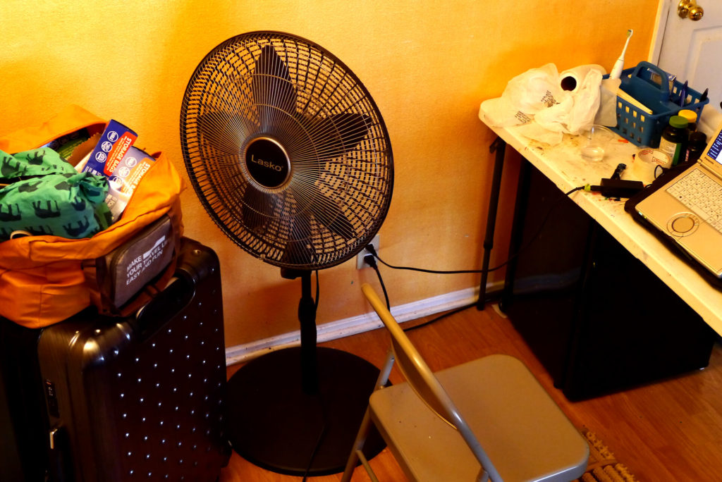 The view of my lonely room in Califonia there are suitcase, fan and the table