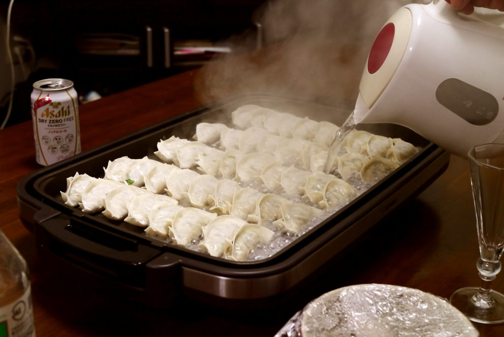 Pouring boiled water in coooking gyoza on hotplate.
