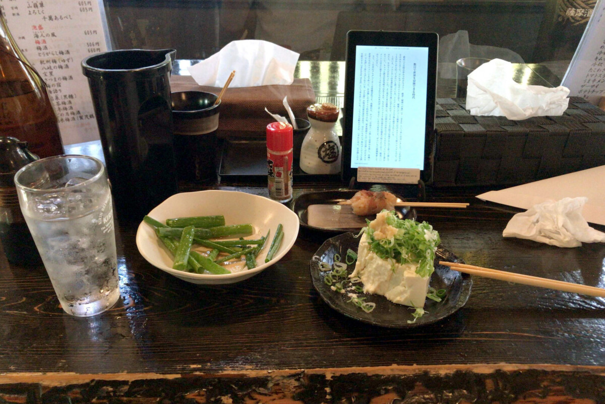izakaya table Tofu, salty negi, and bottle of soju on the table at izakaya Omasa in Hiroshima Japan
