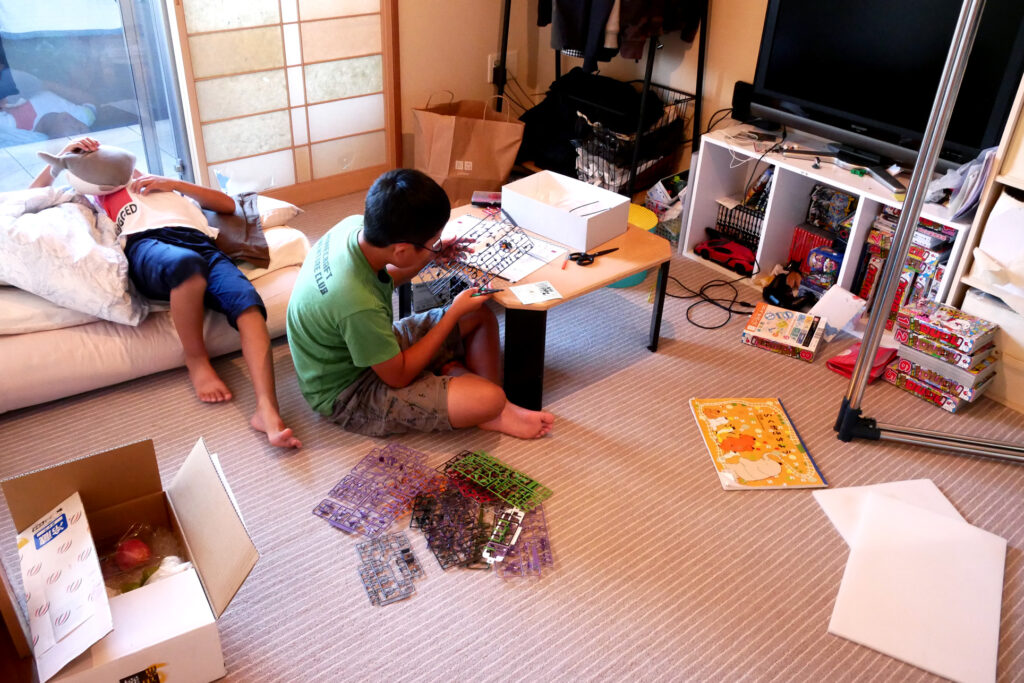 A boy making evangelion plastic model and another boy lying the futon mat in the room in Hiroshima Japan