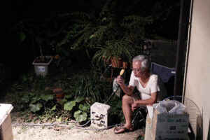 An old Dad is sitting a chair and eating ice candy in the dark night at yard