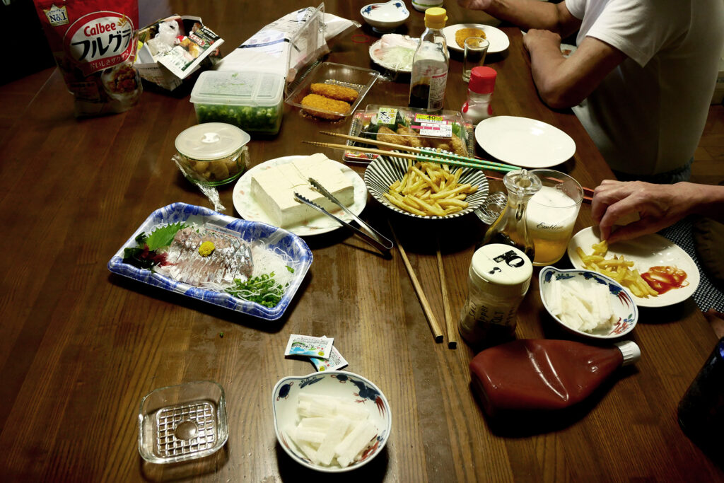 Japanese dishes like sashimi on the wooden table and people are eating fries
