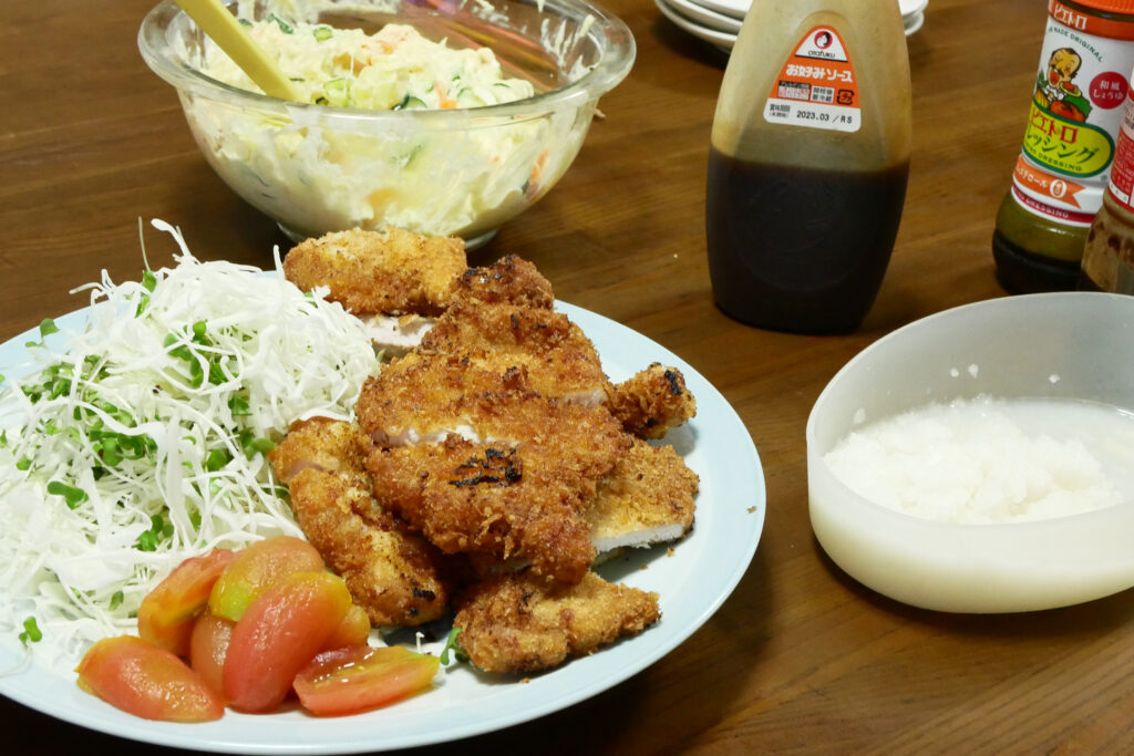 Pork cutlet, potato salad, and bottles of sauce on the wooden table