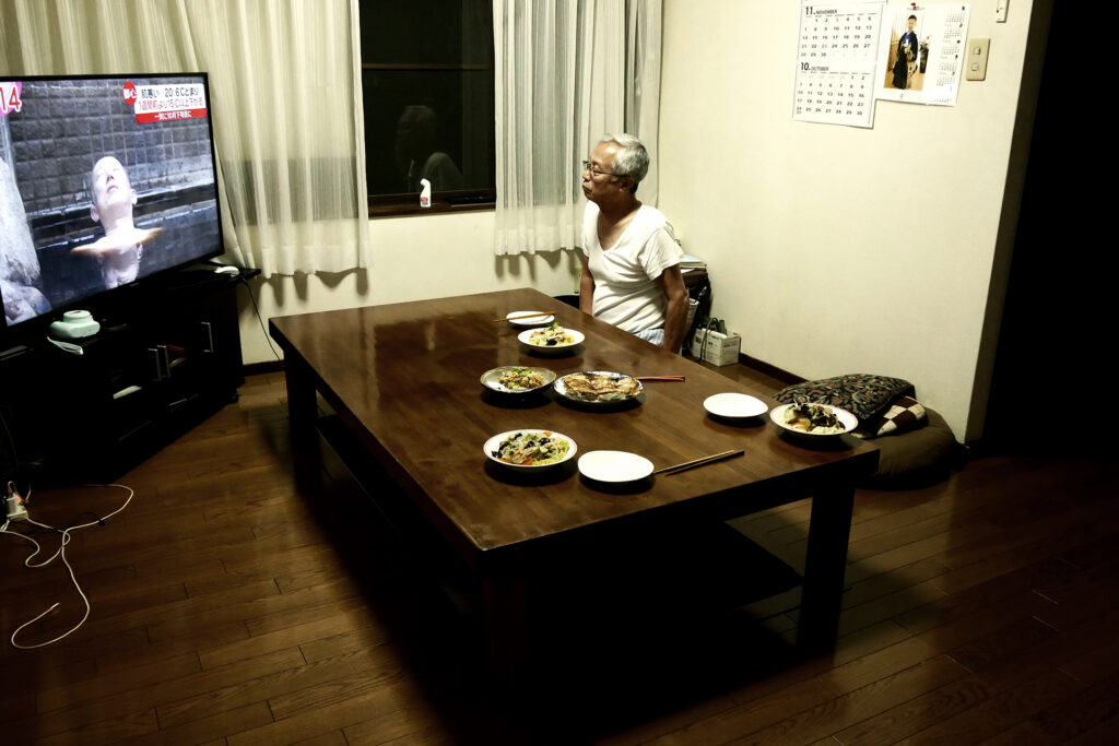 An elder man who is my father is watching TV at a dining room's table