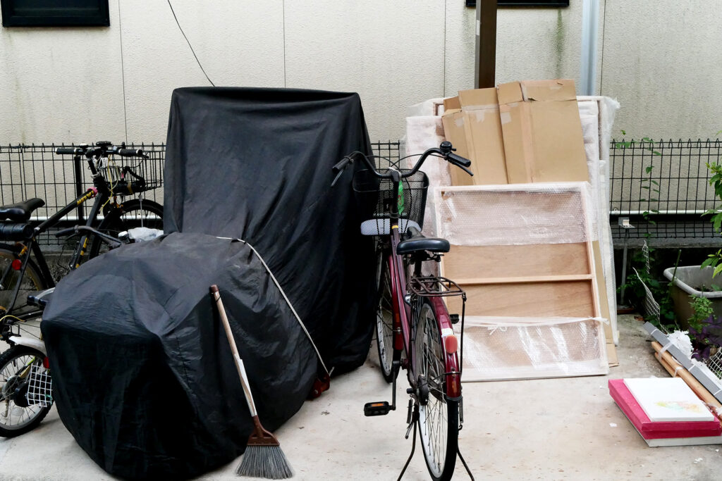 A covered motor bike, a bicycle and paintings on the yard