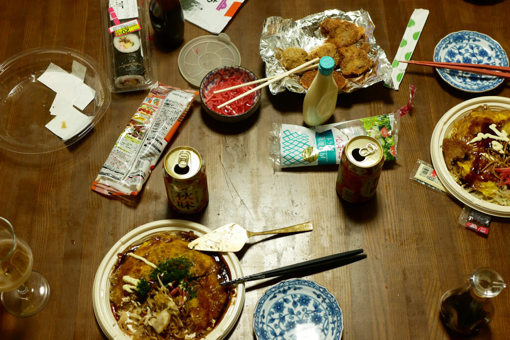 Packed Hiroshima style Okonomiyaki, canned beer, deep fried pork cutlet etc. on the wooden table