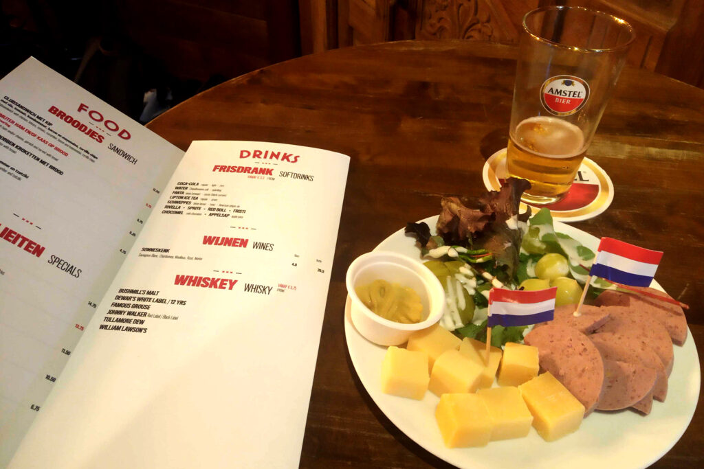 Menu, glass of beer, cheese a and sausage on the plate.