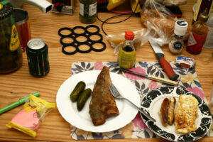 Deep fried fish and eggs, sausages on the plate on the messy wooden table