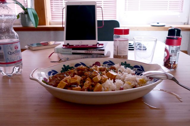 Mapo tofu with rice on the wooden table, there are iPad, seasoning bottles, water