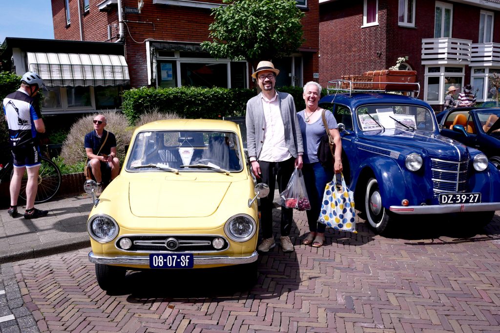 Old cars show, there are two people middle age Japanese and elder dutch lady front of the yellow car in Castricum in the Netherlands
