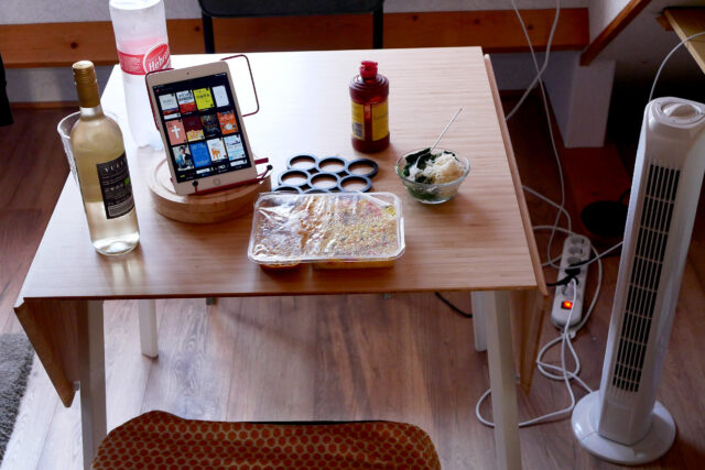 iPad, packed meal, a sauce bottle, and a bottle of white wine on the wooden table