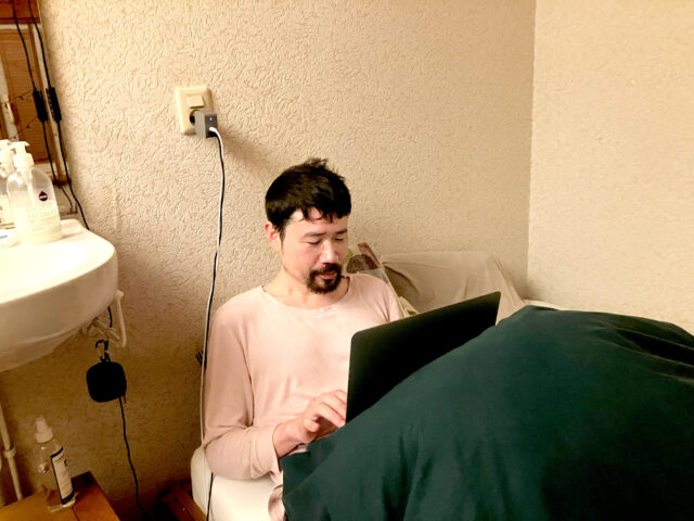 a japanese man handling a laptop in his bed